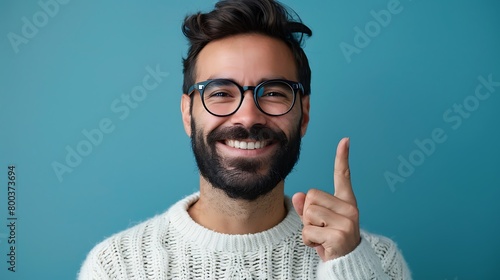 A Young handsome man with beard wearing casual sweater and glasses over blue background smiling and confident gesturing with hand doing small size sign with fingers looking and the camera, Measure photo