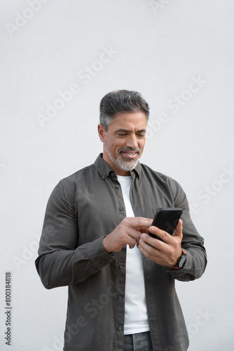 Smiling hispanic business man using smartphone mobile phone device for online financial bank transactions. Freelancer entrepreneur in shirt holding cellphone isolated on white background, vertical