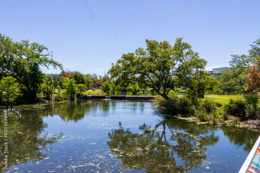 Fototapeta premium a beautiful spring landscape in the Sculpture Garden at New Orleans City Park with a lake, lush green trees, grass and plants, sculptures, people and blue sky in New Orleans Louisiana USA