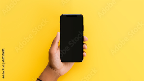 Hand holding smartphone with a black blank screen isolated on a yellow background Copy space Mockup Template for Presentation.
