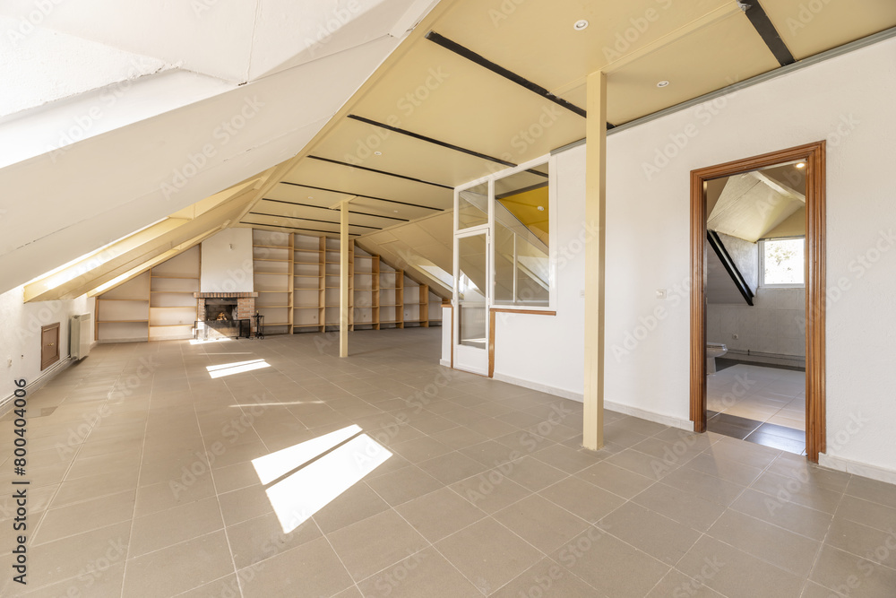 Large attic with a metal column in the center, a wall with shelves and an empty bathroom Large attic with a metal column in the center, a wall with shelves and an empty bathroom