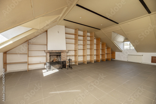 Large attic with wall of shelves  windows with skylights  glass staircase  fireplace and gray floor