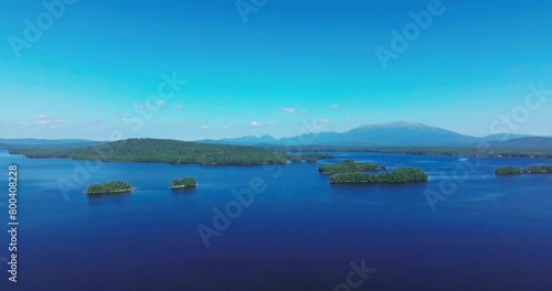 Drone captures calm blue Ambajejus Lake with Mount Katahdin in background against clear sky in Maine with an aerial perspective