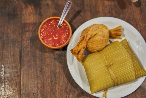 Homemade tamale and humita on a white plate with a red sauce on the side, typical food from the north of Argentina. corn leaves Stuffed corn flour dough photo