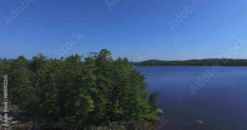 Drone flying around trees surrounded by scenic blue Ambajejus Lake with Mount Katahdin in background against clear sky in Maine photo