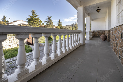 View of the gardens of a house with white balustrades from a long outside terrace with a decorative clay jar photo