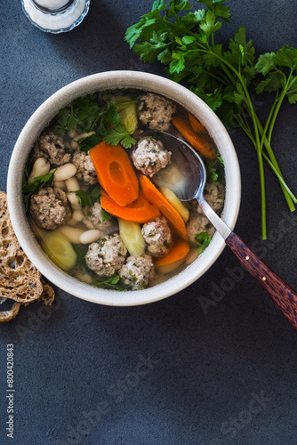 White bean and beef meatball soup with carrots on grey background, directly above