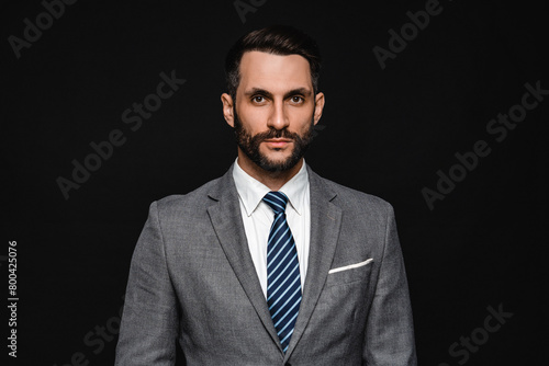 Young handsome businessman wearing tuxedo looking at the camera isolated over black background. Portrait of successful manager CEO boss clerk in business formal suit attire