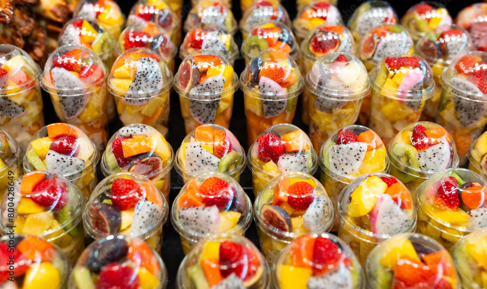 Fruit Salad arranged in plastic cups on a market. Cut and ready fruit ready to sell in market. Convenience, healthy lifestyle. Strawberries, kiwi, melon, pineapple, figs, dragon in a plastic glass.
