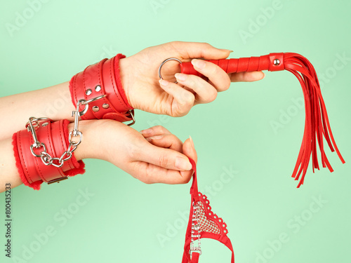 Woman's hands holding red whip for adult role play games and red panty over mint background