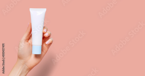 Female hand holding with two fingers a white tube of cosmetics