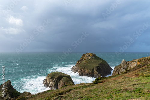 Sous un ciel menaçant, un grain s'approche alors que les falaises et îlots rocheux à la Pointe du Van se dressent majestueusement sur le littoral breton, avec une mer agitée