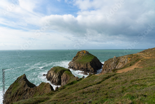 Sous un ciel bleu parsemé de nuages, les falaises et îlots rocheux à la Pointe du Van se dressent majestueusement sur le littoral breton, avec une mer calme. photo