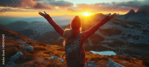 Sunset scene of a young woman in a hoodie rejoicing atop a mountain, arms raised, in a panoramic banner.