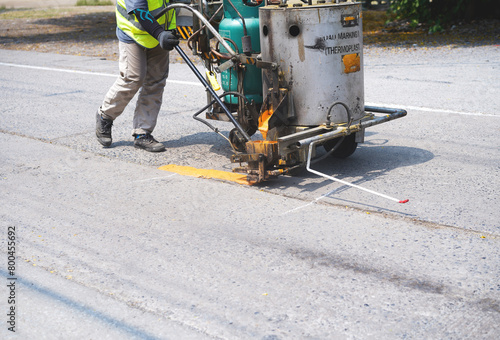 Man use thermoplastic road marking paint machine, hot melt marking paint machinery spraying a yellow line on concrete road. © surasak