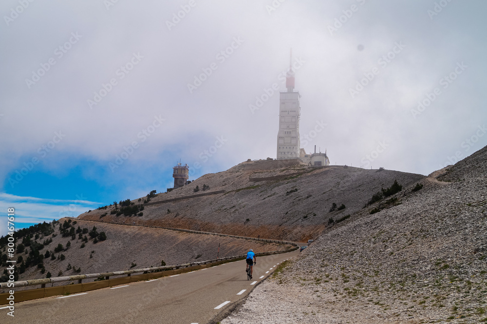 Rear view of cyclist going to the top of Mount Ventoux surrounded by mystical fog in Provence region of southern France, Europe. One of the stages of tour de france. Mountain peak in Luberon range