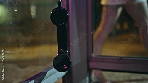 Broken payphone swinging wire at blurred evening city closeup. Telephone hanging