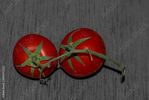 Two fresh red tomatoes with stem still attached on a grey background