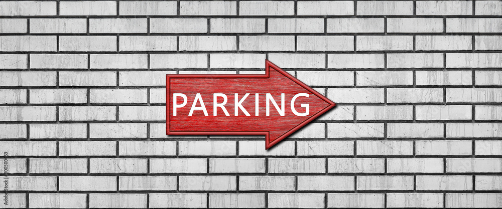 Fototapeta premium Red wooden arrow sign with the inscription PARKING hanging on a white brick wall. Right arrow pointer