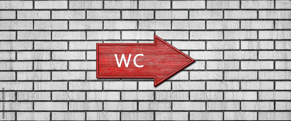 Red wooden arrow sign with the inscription WC hanging on a white brick wall. Right arrow pointer Red wooden arrow sign with the inscription WC hanging on a white brick wall. Right arrow pointer