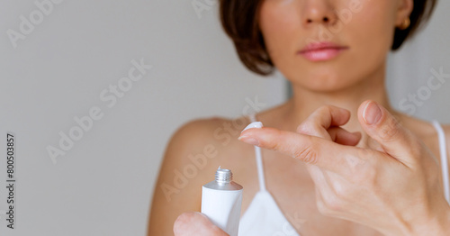 Fototapeta A woman presses the ointment onto her finger and applies it to the bite site by a bedbug on her shoulder on a white background, close-up