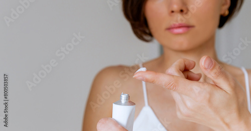 A woman presses the ointment onto her finger and applies it to the bite site by a bedbug on her shoulder on a white background, close-up. Skin health problem. Red pimples. photo