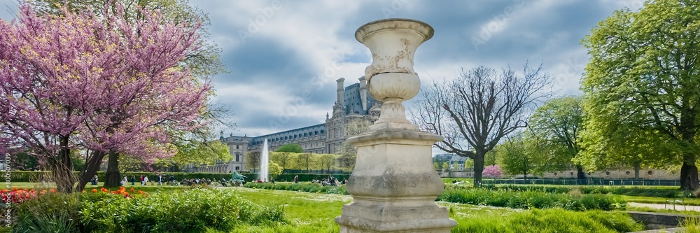 Blooming spring trees and classic vase sculpture in a serene European public garden, with historic architecture in the background  ideal for springtime and travel themes