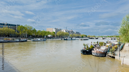 Scenic view of the Seine river and moored boats on a sunny day, with historic Parisian architecture in the background, ideal for travel and tourism themes