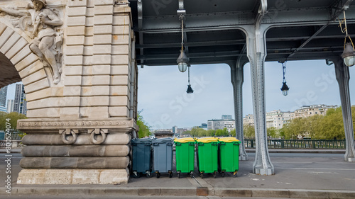 Colorful recycling bins lined up under a bridge in an urban setting, representing waste management and environmental conservation concepts