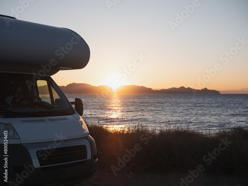 A motor home is parked by the sea at golden hour