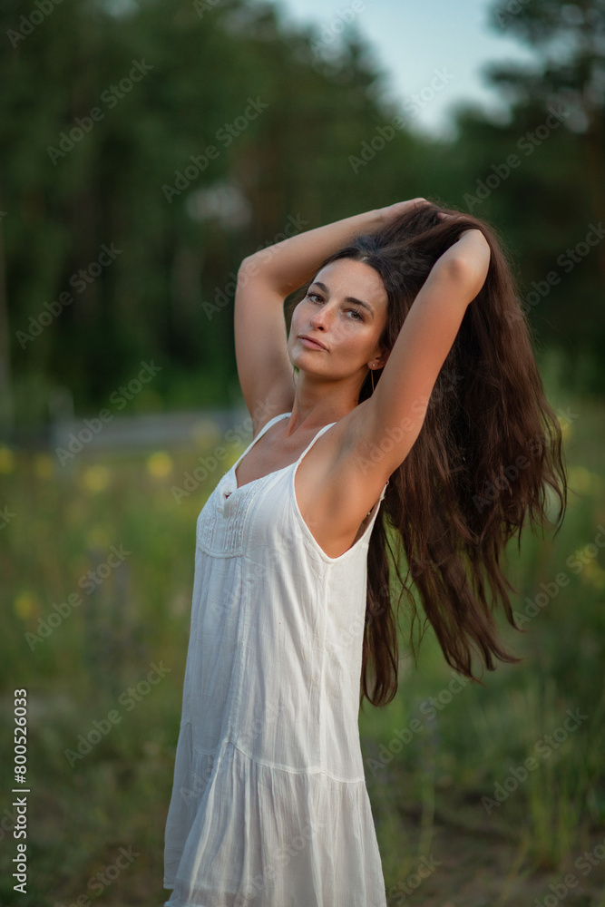 Portrait of a young beautiful dark-haired girl in a light dress in a summer field.