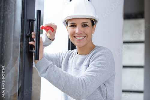 happy woman builder unscrews fastening screws handle window photo