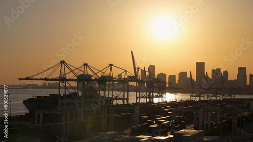 Drone footage of cargo containers and huge cranes by sea and cityscape during bright sunset at Miami port in Florida
