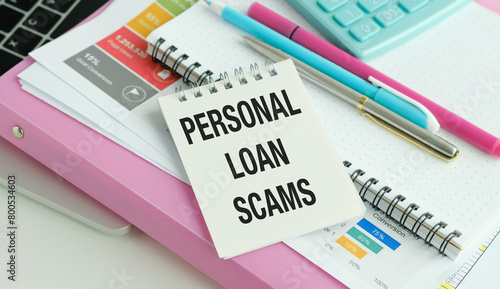 On a wooden table under a black paper clip lies a sheet of white paper with the text Personal Loan Scams.