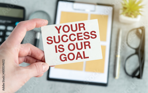 Your success is our goal text on blank business card being held by a woman's hand with blurred background. Business concept to help customers to achieve their goals.