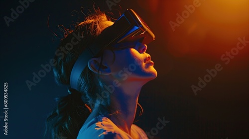 Portrait of young woman wearing VR goggles headset looking up, dark background.