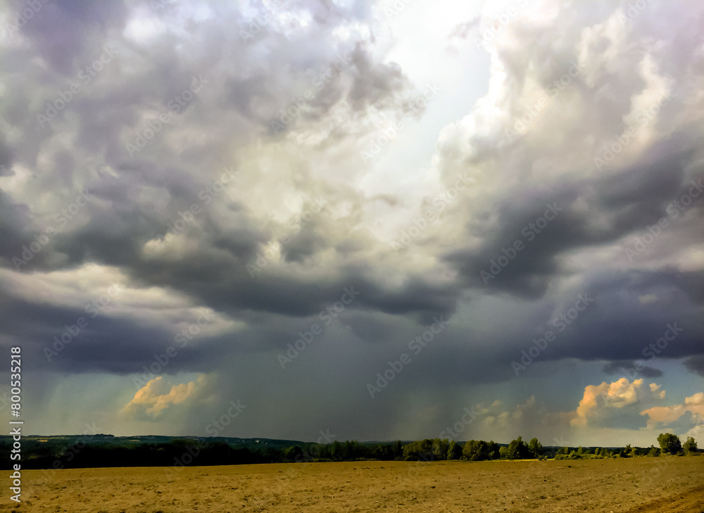 Rain falling from towering clouds on farm fields and forest