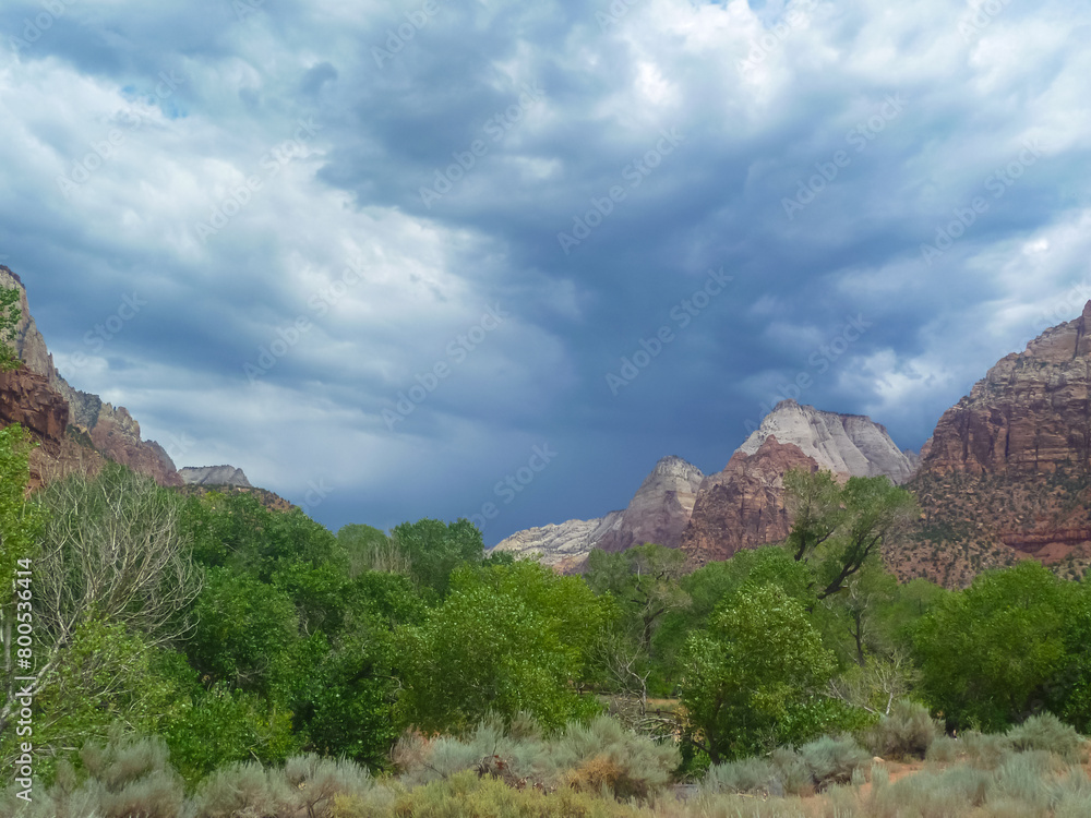 Stormy sky with dark clouds accumulating above Zion National Park Canyon, Utah, USA. Uninhabited canyon with majestic rock formations, steep cliffs, mountains and trees. Bad weather building up