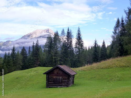 Picturesque landscape of the mountain slope in bright colors. In the foreground is an old wooden barn on the grass.