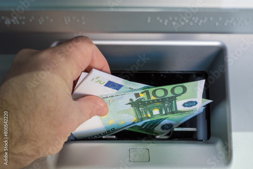 a man's hand puts euro bills in the ATM tray to be credited to the account. mortgage repayment concept