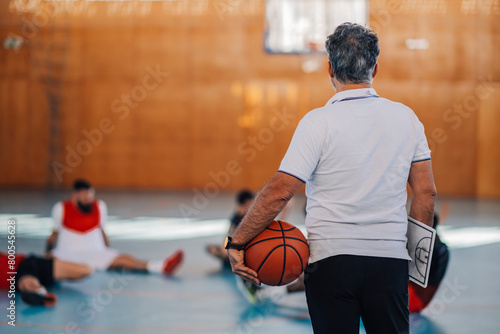 Rear view of an elderly male basketball coach holding a ball during practice