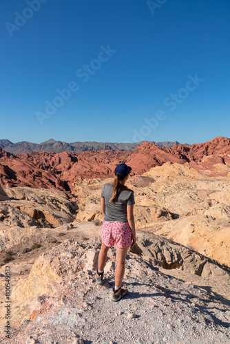 Rear view of woman at Silica Dome viewpoint overlooking the Valley of Fire State Park in Mojave desert, Nevada, USA. Landscape of Aztek sandstone rock formations. Hot temperature in arid vegetation