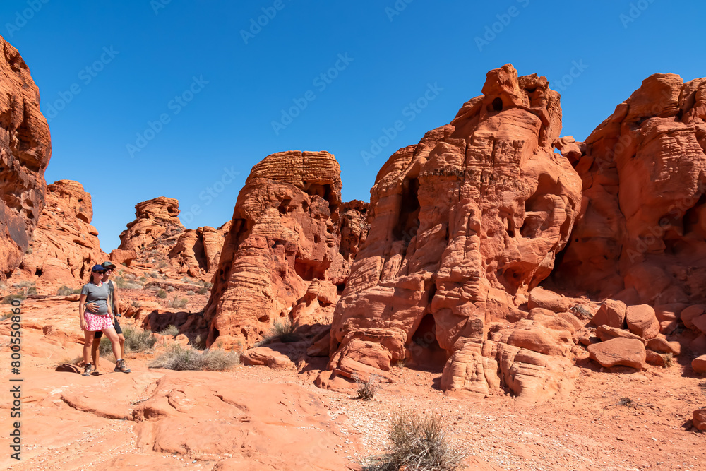 Couple at the entrance of windstone arch (fire cave) in Valley of Fire State Park, Mojave desert, Nevada, USA. Scenic view of beehive shaped red sandstone rock formations. Barren deserted landscape Couple at the entrance of windstone arch (fire cave) in Valley of Fire State Park, Mojave desert, Nevada, USA. Scenic view of beehive shaped red sandstone rock formations. Barren deserted landscape