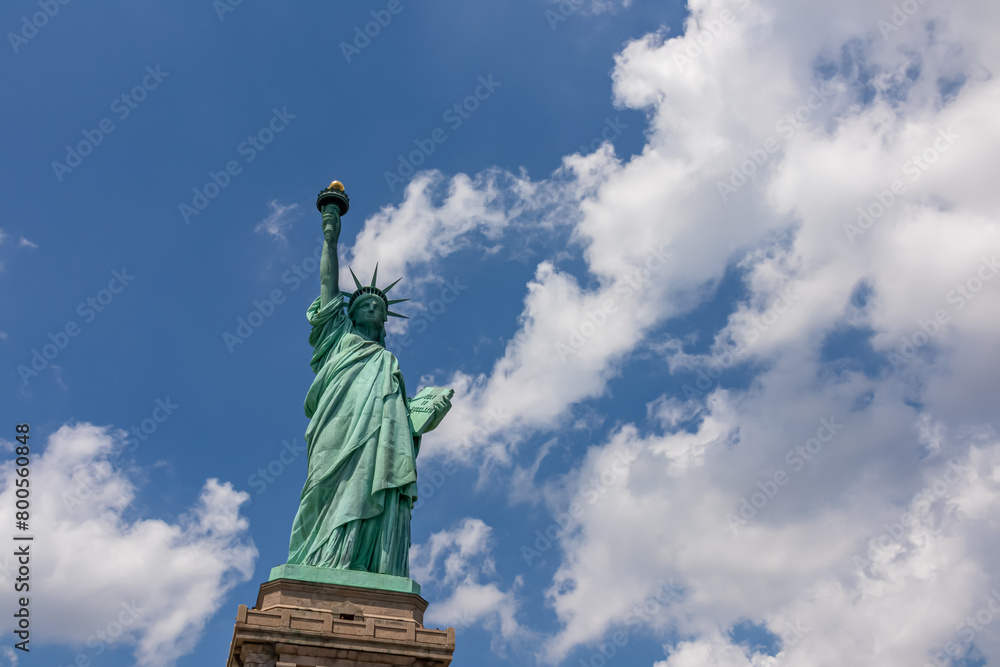 Fototapeta premium A close up on an iconic representation of freedom and independence, the Statue of Liberty with flaming torch on Liberty Island. The Lady on a Pedestal is surrounded by clouds. American history.