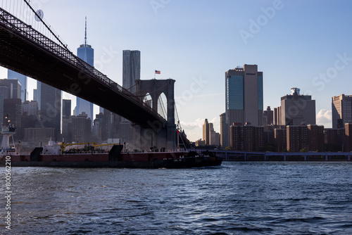 Iconic Brooklyn Bridge connecting New York City s urban landscape with stunning skyline and architectural marvel. Tall skyscrapers in the back. American flag on top of a gate waving gently.