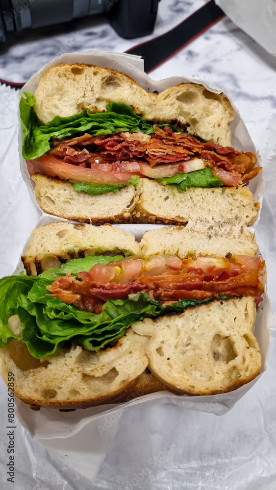 Typical New Yorker bagel with green salad, roasted beacon, and other ingredients on sesame bagel, prepared in a take-away foil. Nutritious breakfast. Typical New Yorker bagel with green salad, roasted beacon, and other ingredients on sesame bagel, prepared in a take-away foil. Nutritious breakfast.