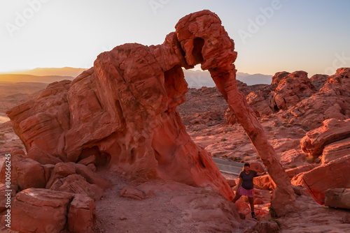Obraz na płótnie Tourist woman standing next to elephant shaped Aztec Sandstone Rock formations during sunrise in Valley of Fire State Park in Mojave desert near Overton, Nevada, USA. Red rocks and stone desert w salonie