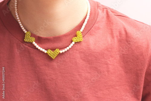 Handicraft beads made from imitation pearls with heart green pendants on a woman in a t-shirt.
