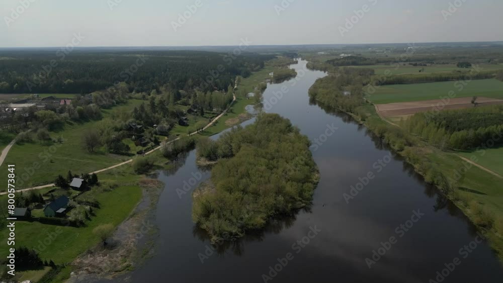 Drone view of a river among fields and forests on a sunny day with countryside houses on its bank Drone view of a river among fields and forests on a sunny day with countryside houses on its bank