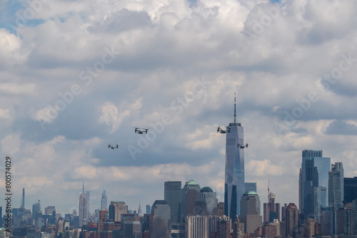 A formation of drones flying across the sky with captivating New York urban skyline with striking and modern skyscrapers seen from The Liberty Island. Think clouds above the city. Protection